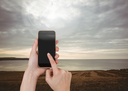 Digital composite of Hand Touching Mobile phone with evening sky landscape