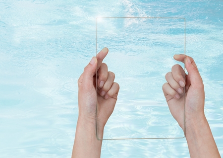 Digital composite of Hand holding glass screen over clear blue waterの写真素材