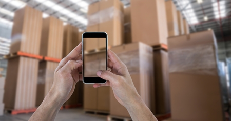 Digital composite of Hands photographing boxes through smart phone in warehouseの写真素材