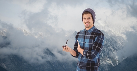 Digital composite of Male hipster holding smoking pipe against fog covering mountains