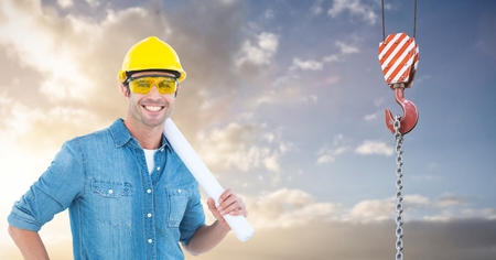 Digital composite of Smiling architect holding blueprints by crane hook