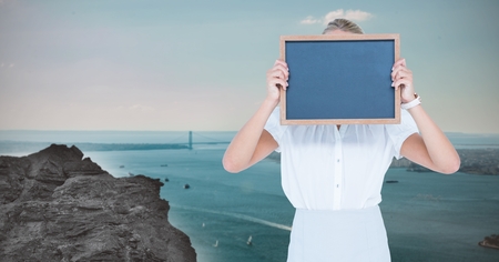 Digital composite of Woman hiding face with slate against riverの写真素材