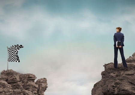 Digital composite of Businessman looking at checked flag on rock against skyの写真素材