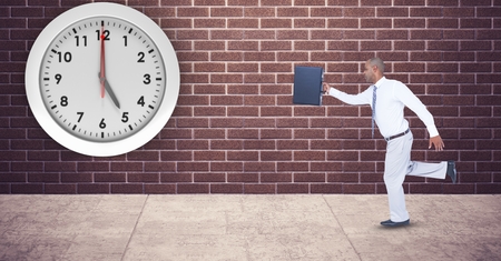 Digital composite of Businessman with briefcase running late with clock mounted on wallの写真素材