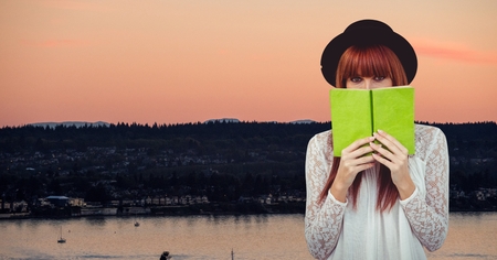 Digital composite of Female hipster holding book at lake shoreの写真素材