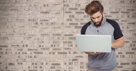 Digital composite of Hipster using laptop against wall