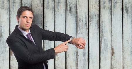 Digital composite of Portrait of angry businessman showing time on wristwatch against wooden wallの写真素材