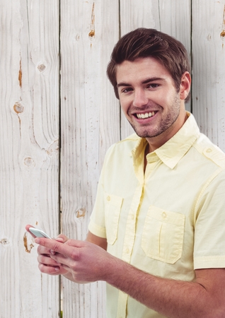 Digital composite of Portrait of happy male hipster holding smart phone against wooden wallの写真素材