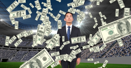 Digital composite of Money falling on businessman at football stadium representing corruptionの写真素材