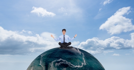 Digital composite of Businessman meditating on globe against skyの写真素材