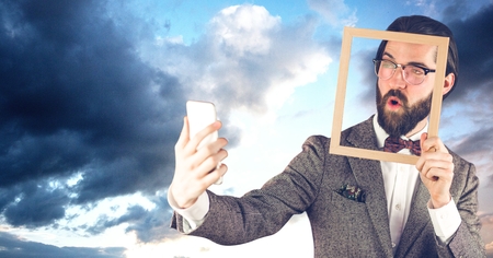 Digital composite of Hippie businessman holding frame while taking selfie on smart phoneの写真素材