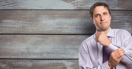 Digital composite of Portrait of confident businessman buttoning sleeve against wooden wallの写真素材
