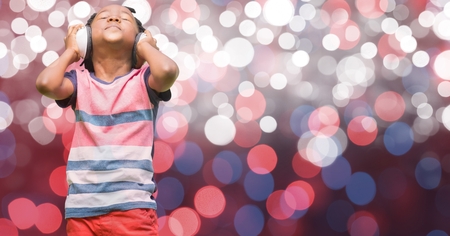 Digital composite of Boy listening music through headphones over glowing bokeh