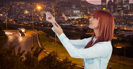 Digital composite of Redhead woman with arms raised in city