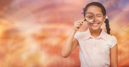 Digital composite of Happy girl looking through magnifying glass over bokehの写真素材