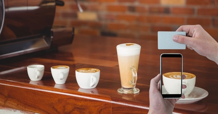 Digital composite of Hand photographing cup of cappuccino with smart phone while holding card in coffee shopの写真素材