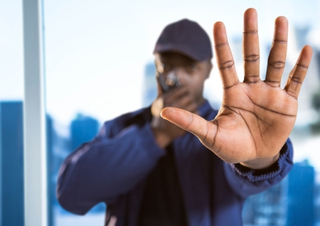 Digital composite of Security guard with walkie talkie and hand in front against blurry window showing cityの写真素材
