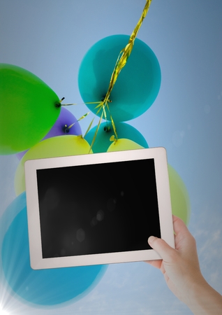 Digital composite of Hand with tablet against baloons and flareの写真素材