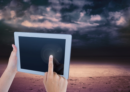 Digital composite of Hand touching tablet with dark cloudy sky