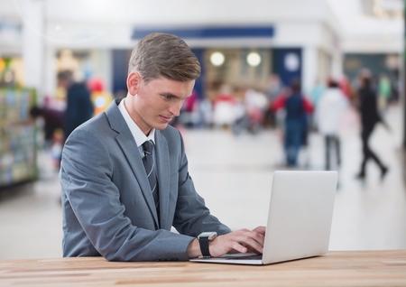Digital composite of Businessman on laptop in shopping mallの写真素材
