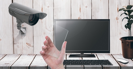 Digital composite of Hand holding glass screen with Security camera watching laptopの写真素材