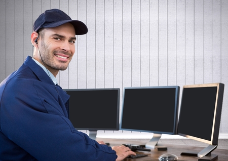 Digital composite of security guard smiling in front of the computers with white wood background