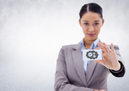 Digital composite of Business woman holding out card showing grey cloud and gear graphic against white wallの写真素材
