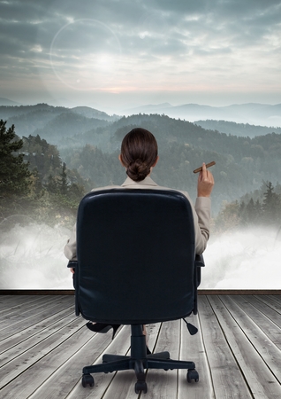 Digital composite of Businesswoman Back Sitting in Chair with cigar and landscapeの写真素材