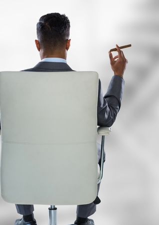 Digital composite of Back of seated business man smoking cigar against blurry grey stairsの写真素材