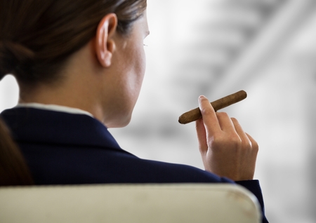 Digital composite of Over shoulder business woman smoking cigar against blurry grey stairsの写真素材