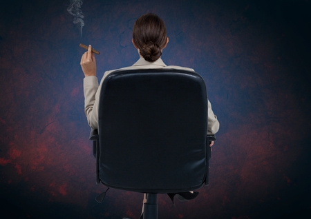 Digital composite of Businesswoman Back Sitting in Chair with cigar and dark backgroundの写真素材