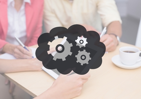 Digital composite of People at table with tablet behind grey cloud and gear graphicの写真素材