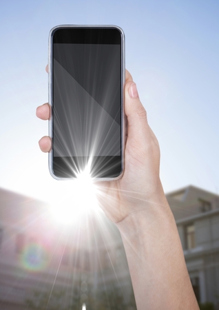 Digital composite of Hand with phone against blurry building with flareの写真素材