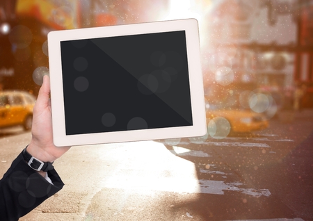 Digital composite of Hand with tablet against blurry street with bokeh and flaresの写真素材
