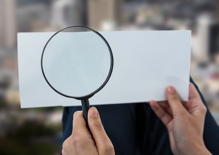 Digital composite of Magnifying glass in hands looking at paper over cityの写真素材