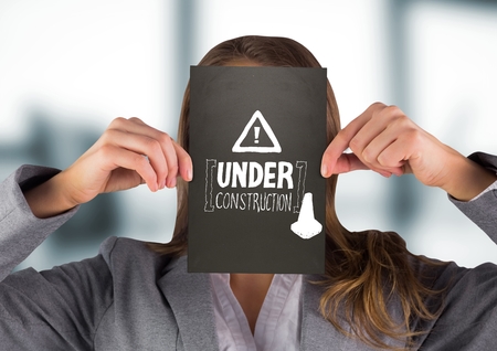 Digital composite of Business woman with black card over face showing white construction doodle against blurry grey officの写真素材