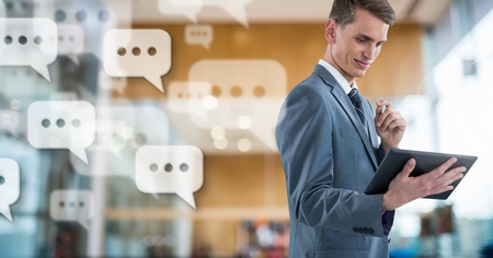 Digital composite of Businessman holding tablet with apps chat messages in large modern hallの写真素材