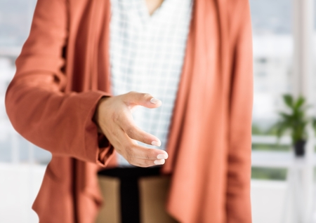 Digital composite of woman with orange blazer giving hand to handshake in her office