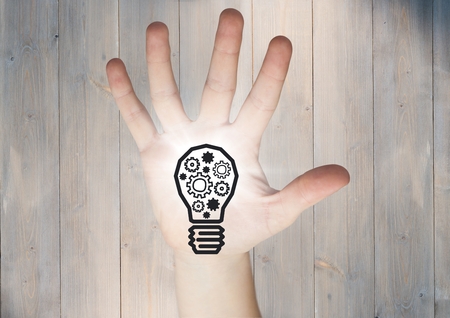 Digital composite of Hand with cogs in lightbulb graphic and flare in palm against grey wood panelの写真素材