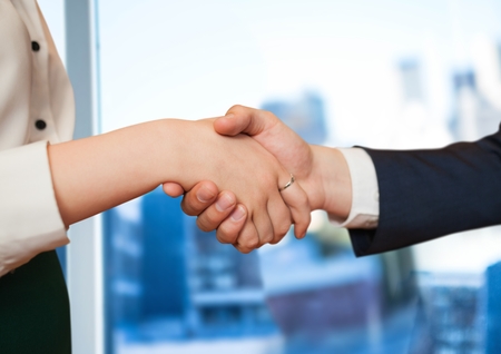 Digital composite of foreground of handshake in front of the window of the office