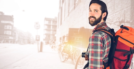 Digital composite of Hipster carrying backpack with camera standing against buildingsの写真素材