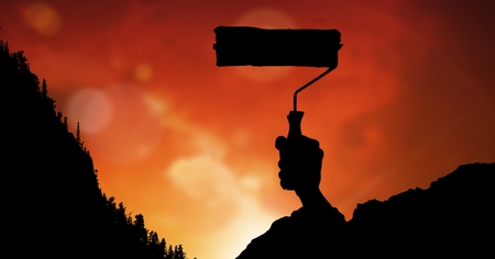Digital composite of Silhouette image of hand holding paint roller against red skyの写真素材