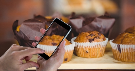 Digital composite of Hand photographing muffins through smart phone at bakeryの写真素材