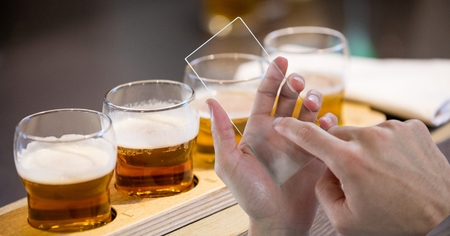 Digital composite of Hands taking picture of beer glasses through transparent device at bar