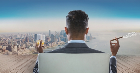 Digital composite of Rear view of businessman sitting on chair with glass of alcohol and smoking cigar while looking at cの写真素材