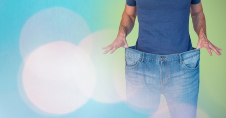 Digital composite of Mid section of man holding loose jeans representing weight loss and standing...