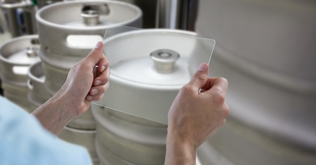 Digital composite of Cropped hands photographing kegs through transparent device at breweryの写真素材
