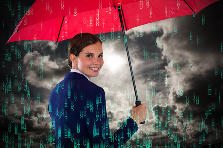 Portrait of smiling businesswoman holding red umbrella against dark sky with white cloudsの写真素材