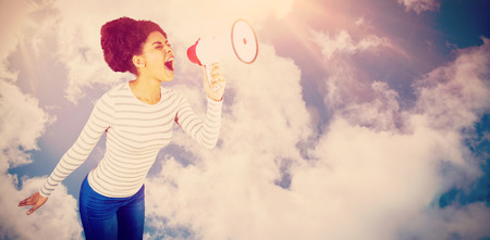 Carefree young woman yelling with megaphone  against bright blue sky with cloudsの写真素材