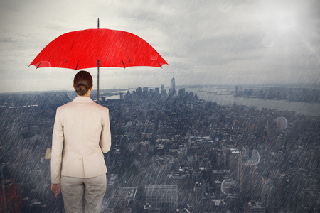 Rear view of female executive carrying red umbrella against new yorkの写真素材